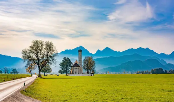 Beautiful autumn scenery with St. Coloman Pilgrimage Church and hazy alpine ranges on background. Schwangau, Germany. Baroque church near famous Neuschwanstein castle. Popular travel destination