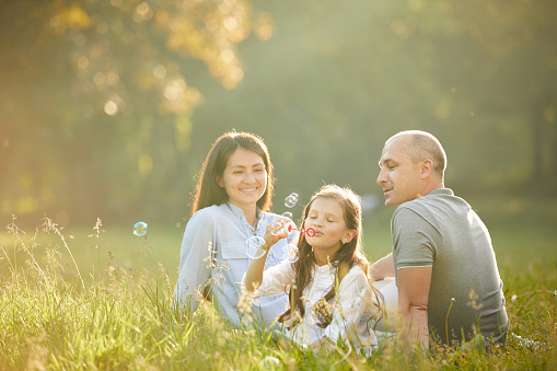 happy family with child girl playing with soap bubble on meadow