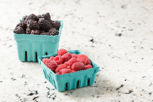 Fresh and ripe blackberries and raspberries from the farmers market in blue paper boxes on marble background