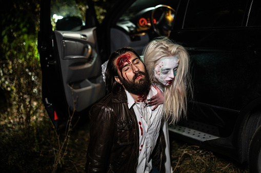 Female zombie holding her victim after biting him at neck