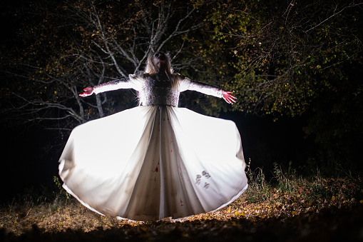 Woman dressed as witch standing in forest with arms outstretched during night