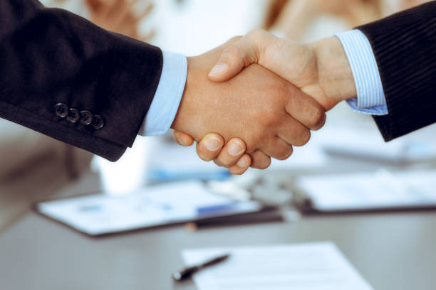 istock Business people shaking hands at meeting while theirs colleagues clapping and applauding. Group of unknown businessmen and women in modern white office. Success teamwork, partnership and handshake concept 1249775909