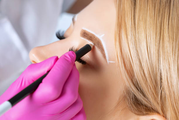 istock Woman Having Permanent Make-up Tattoo on her Eyebrows.Permanent make-up for eyebrows in beauty salon. Closeup beautician doing tattooing eyebrow. Professional makeup and cosmetology skin care. 1249779013