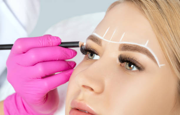 istock Woman Having Permanent Make-up Tattoo on her Eyebrows.Permanent make-up for eyebrows in beauty salon. Closeup beautician doing tattooing eyebrow. Professional makeup and cosmetology skin care. 1249779072