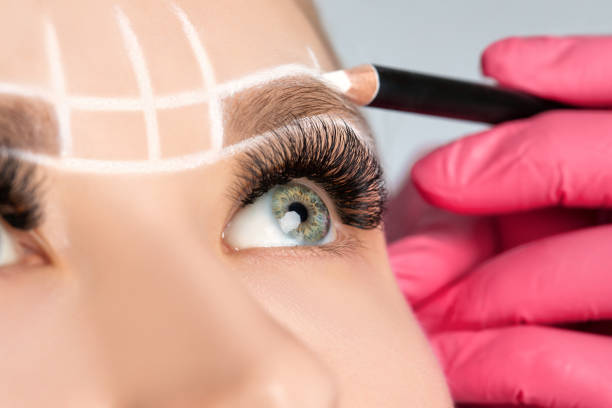 istock Woman Having Permanent Make-up Tattoo on her Eyebrows. Closeup beautician doing tattooing eyebrow. Green eyes close up. Professional makeup and cosmetology skin care. 1249779117