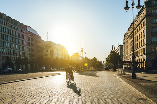 rear view on two cyclists going on Berlin street Unter den Linden, in the background the Television tower in the backlit of the early morning sun