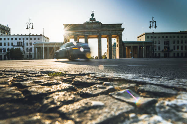 car is passing Brandenburger Tor at sunrise hour single car is passing in front of Brandenburger Tor in the backlit of early morning sun city gate stock pictures, royalty-free photos & images