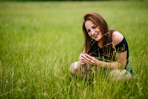 Portrait of pretty young Caucasian woman crouching in grass.