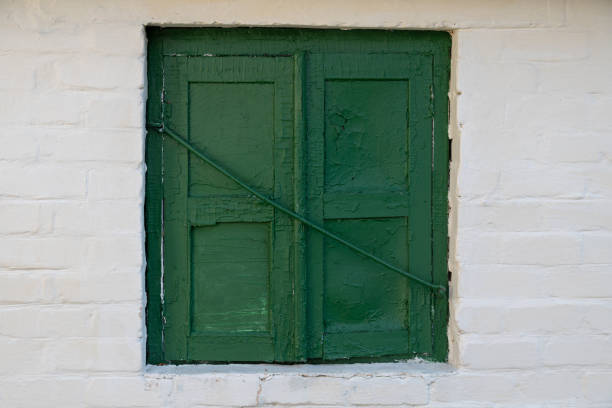 istock Old green window with peeling paint on a white brick wall. 1249784727