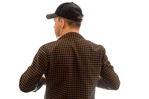 A thirty-forty-year-old man in a baseball cap and a plaid shirt stands with his back