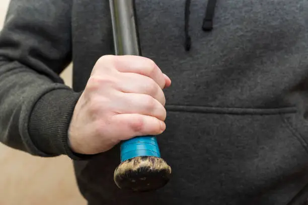 Powerful man’s hand in a hoodie grips the shabby hilt of a black wooden baseball bat