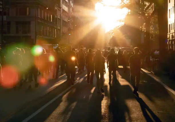 Crowd of people walking down the street into the bright light of sunset in New York City NYC