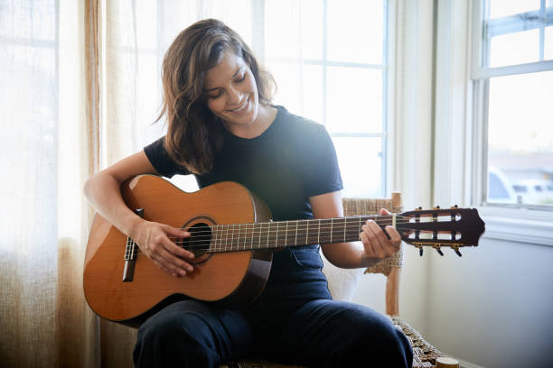 istock Smiling young woman playing a guitar at home 1249797620
