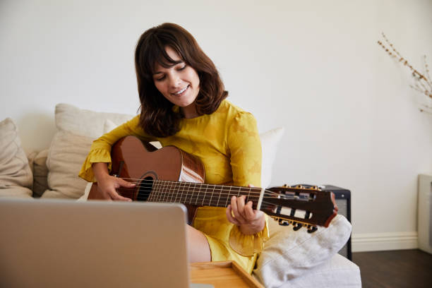 istock Smiling young woman learning guitar online with a laptop 1249798918