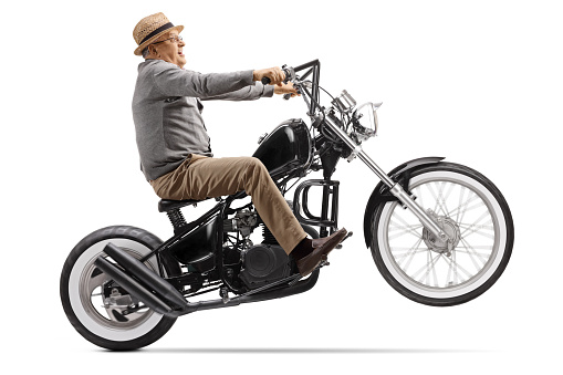 Elderly man rolling a chopper motorbike on the back wheel isolated on white background