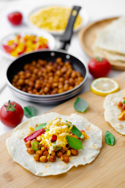 tortilla tacos with chickpeas, bell peppers, corn, tomatoes, basil leaves, green chili topped with cheddar and monterrey jack. on the background are ingredients, lemons, chickpeas in a small pan - mexico chili pepper bell pepper pepper imagens e fotografias de stock