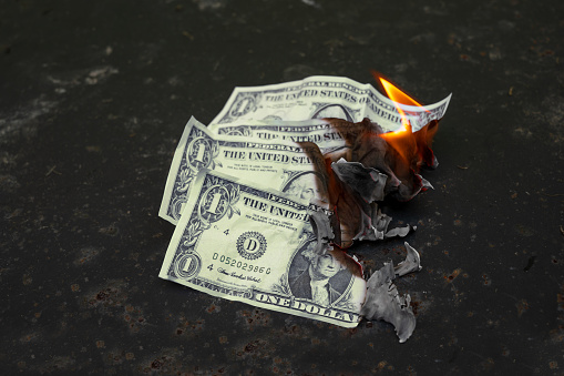 Burning dollar bills, money concept for wage reduction, economic crisis, stock market crash or inflation, dark background with copy space, selected focus, narrow depth of field