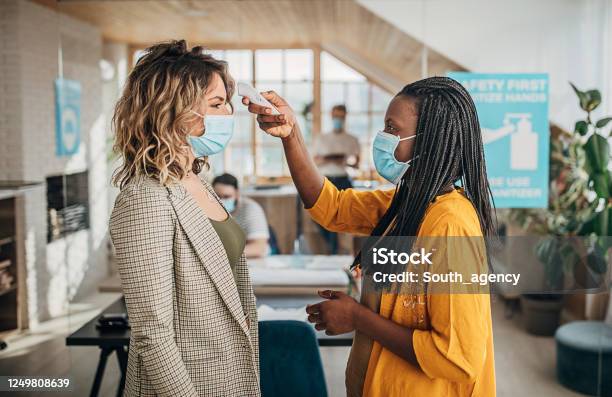 Two Women Using Infrared Thermometer For Measuring Temperature Before Entrance In Office Stock Photo - Download Image Now