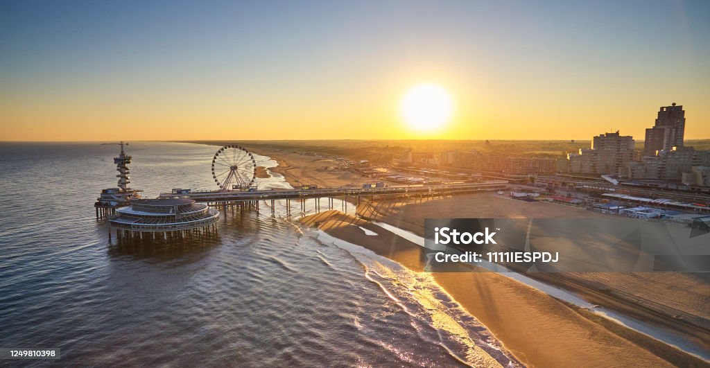 The Pier in Scheveningen The Pier in Scheveningen, the Netherlands during sunrise. The beach is still empty because it’s early in the morning. the skyline of the city can be seen. The picture is taken from the seaside. Scheveningen Stock Photo