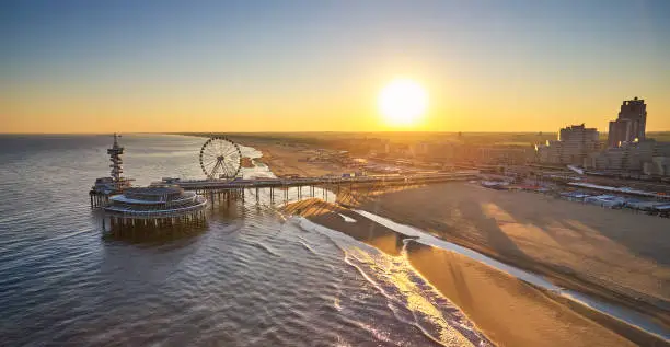 The Pier in Scheveningen, the Netherlands during sunrise. The beach is still empty because it’s early in the morning. the skyline of the city can be seen. The picture is taken from the seaside.