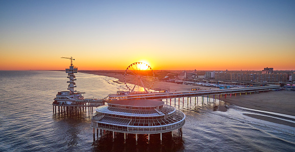 The Pier in Scheveningen, the Netherlands during sunrise. The beach is still empty because it’s early in the morning. the skyline of the city can be seen. The picture is taken from the seaside.