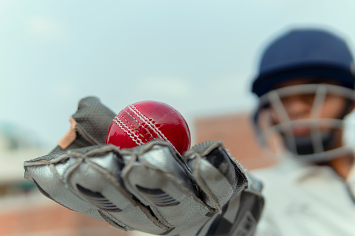 Indian boy in cricket uniform and wearing keeper gloves with hold leather ball. and doing practice. outdoor shoot. copy space.