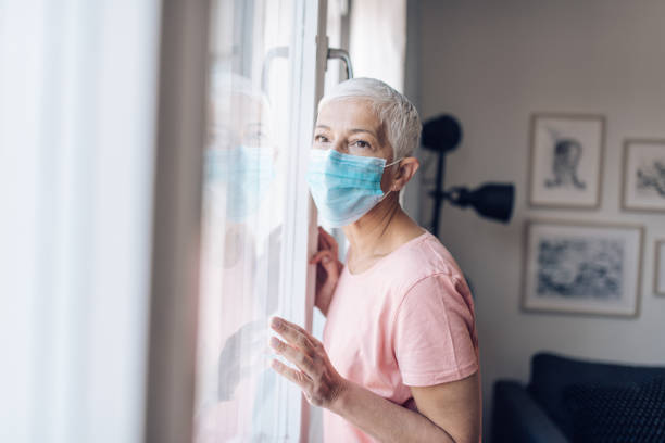 istock Senior woman with a face mask looking through the window 1249813455
