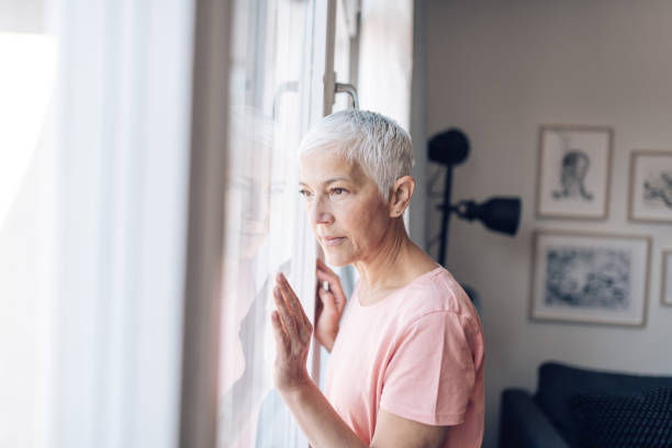 istock Senior woman looking sadly through the window 1249813461