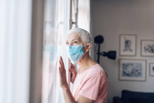 istock Alone senior woman with a face mask looking through the window 1249813463