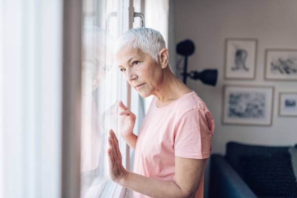 istock Alone senior woman looking through the window 1249813465