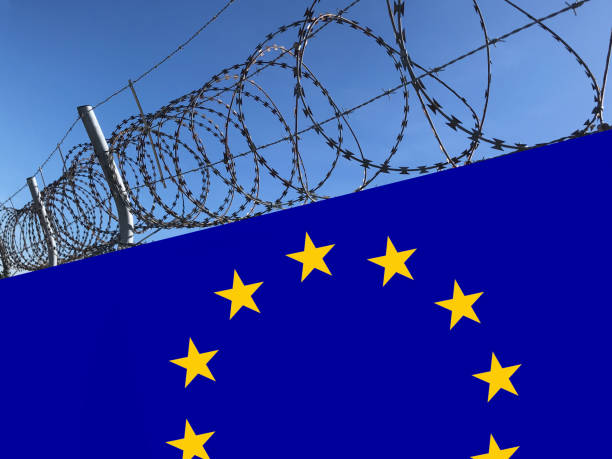 istock Barbed wire steel on wall made from the European Union EU flag. Border control and immigration and refugee politics. 1249816677