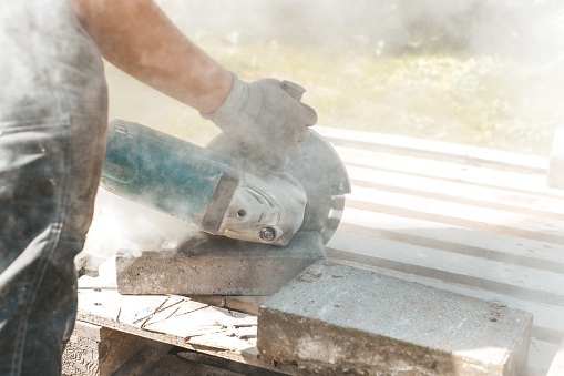 Worker using circular saw for cutting concrete block for road or pavement construction