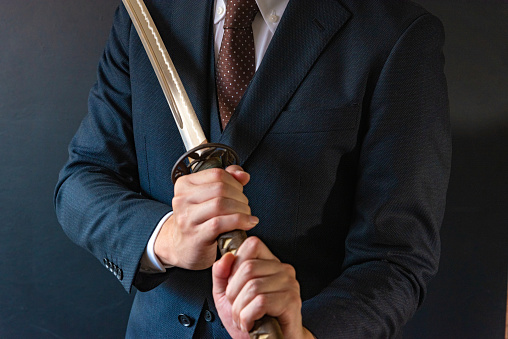 A business man wearing suits and holding japanese sword.