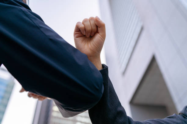Close-up business people's hands while doing elbow bump greeting A low angle close-up business people's hands while doing elbow bump greeting in front of a office building in a business and finance town low angle street japan stock pictures, royalty-free photos & images