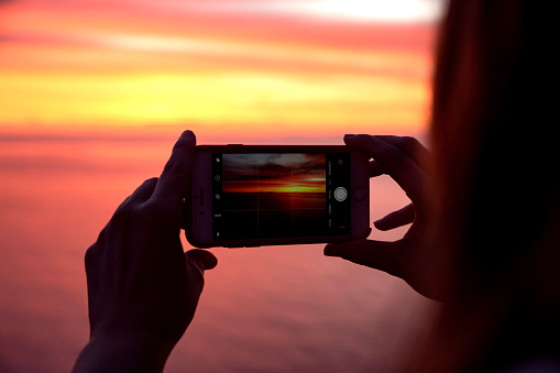 woman taking a photo of a beautiful sunset with a phone