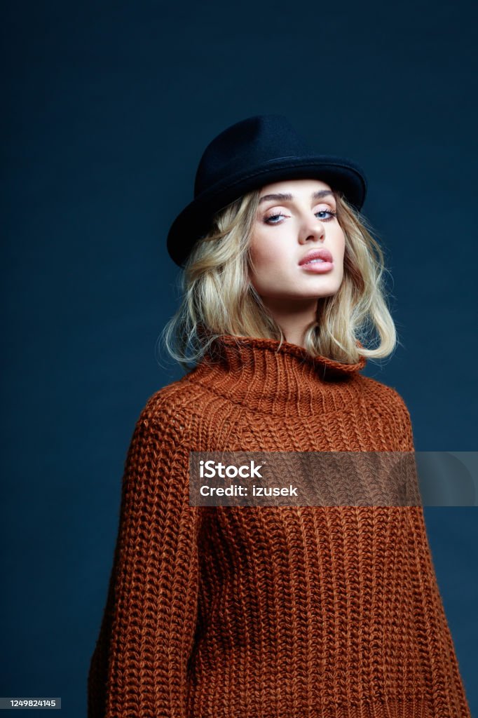 Autumn portrait of blond hair woman in brown sweater Fashion portrait of long hair blond young woman wearing brown sweater and black hat, looking at camera. Studio shot against black background. 20-29 Years Stock Photo
