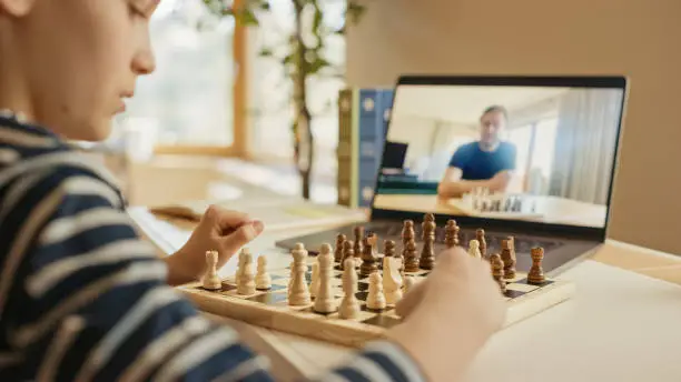 Brilliant Little Boy Playing Chess with His Distant Relative or Uncle, Uses Laptop for Video Call. Remote Online Education, E-Education, Communication with Family, Homeschooling.