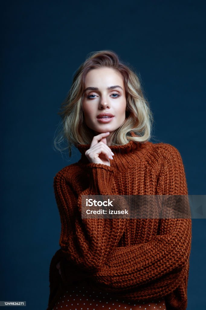 Fashion portrait of blond hair elegant woman in brown sweater Fashion portrait of long hair blond young woman wearing brown sweater, looking at camera. Studio shot against black background. Elegance Stock Photo