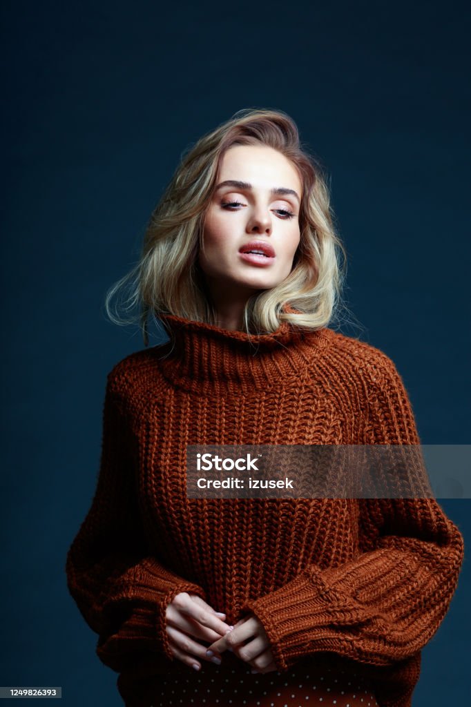 Fashion portrait of blond hair woman in brown sweater Fashion portrait of long hair blond young woman wearing brown sweater, looking away. Studio shot against black background. Fashion Stock Photo