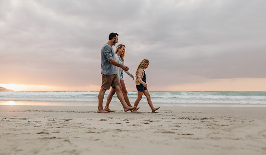 Family of three walking together on a beach vacation. Couple with their daughter on evening walk along the beach.