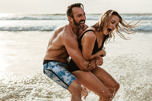 Playful couple having fun on their summer vacation. Man and woman playing on the beach.