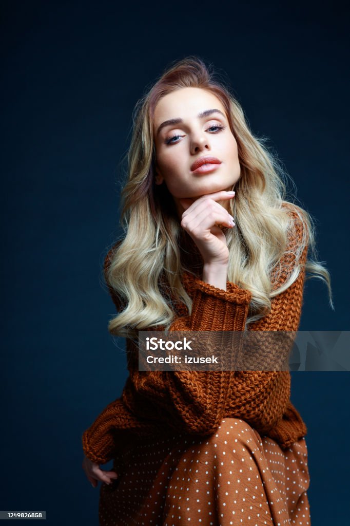 Fashion portrait of elegant woman in brown clothes Fashion portrait of long hair blond young woman wearing brown sweater and skirt, smiling at camera. Studio shot against black background. Knitted Stock Photo