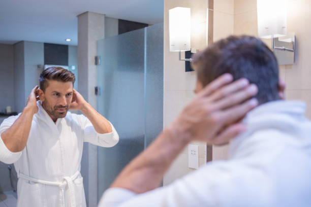 Caucasian man after shower styling his hair in the bathroom Confident Man standing in front of the bathroom mirror and styling his hair vanity mirror photos stock pictures, royalty-free photos & images