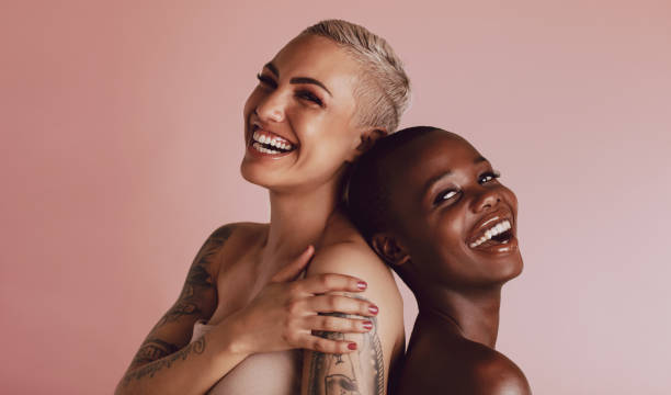 Beautiful women with buzz cut hairstyle smiling at camera Two women with buzz cut hairstyle standing back to back and smiling at camera. Female models with beautiful skin smiling together over beige background. beauty in nature stock pictures, royalty-free photos & images