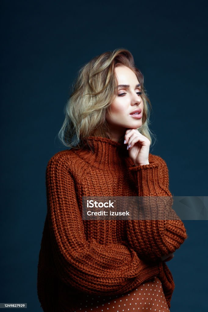 Fashion portrait of elegant woman in brown sweater Fashion portrait of long hair blond young woman wearing brown sweater, looking away. Studio shot against black background. Dark Stock Photo