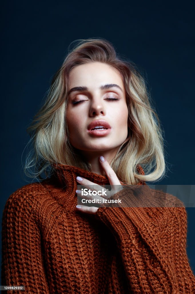Headshot of blond hair woman in brown sweater Fashion portrait of long hair blond young woman wearing brown sweater. Studio shot against black background. Black Color Stock Photo