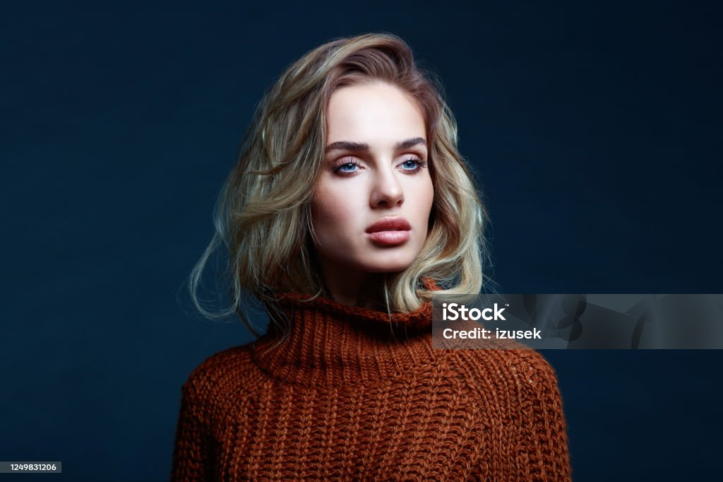 Headshot of blond hair woman in brown sweater Fashion portrait of long hair blond young woman wearing brown sweater, looking away. Studio shot against black background. One Woman Only Stock Photo