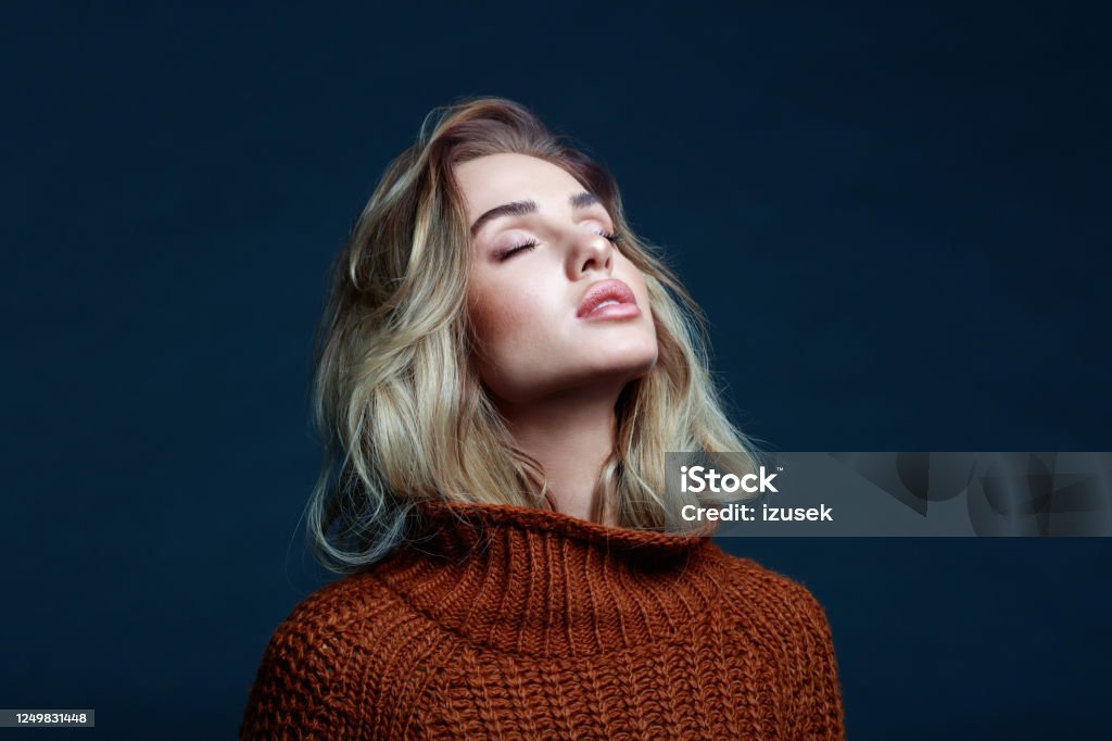 Headshot of blond hair woman in brown sweater Fashion portrait of long hair blond young woman wearing brown sweater. Studio shot against black background. Women Stock Photo