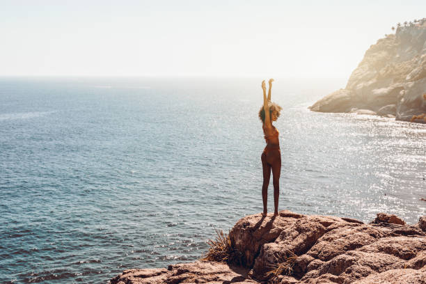 istock Afro girl on rock with raised hands 1249833331