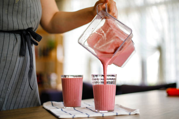 jeune femme versant le milkshake de fraise du mélangeur - yogurt jar cream milk photos et images de collection